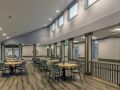 A spacious dining area with tables and chairs, featuring large windows letting in natural light.