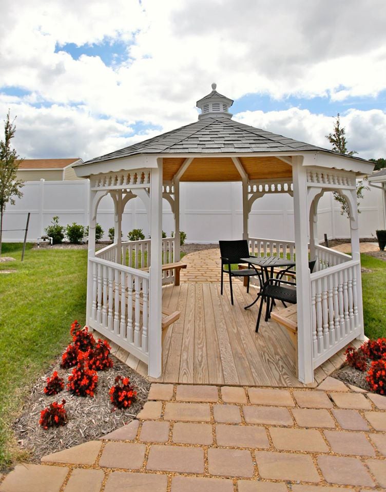 A charming white gazebo in a landscaped garden with flowers and outdoor seating.