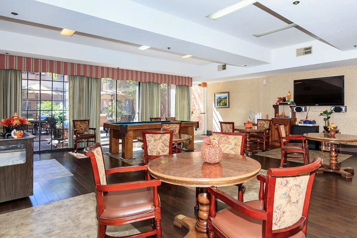 A spacious community room with tables and chairs, featuring large windows and a recreation area.