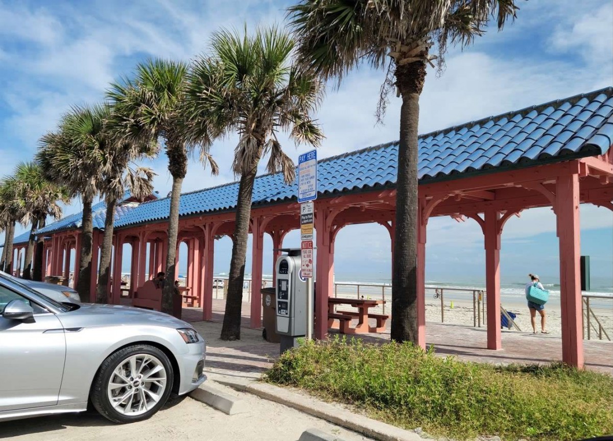 A sunny beachside scene with palm trees, a boardwalk, and parked cars.