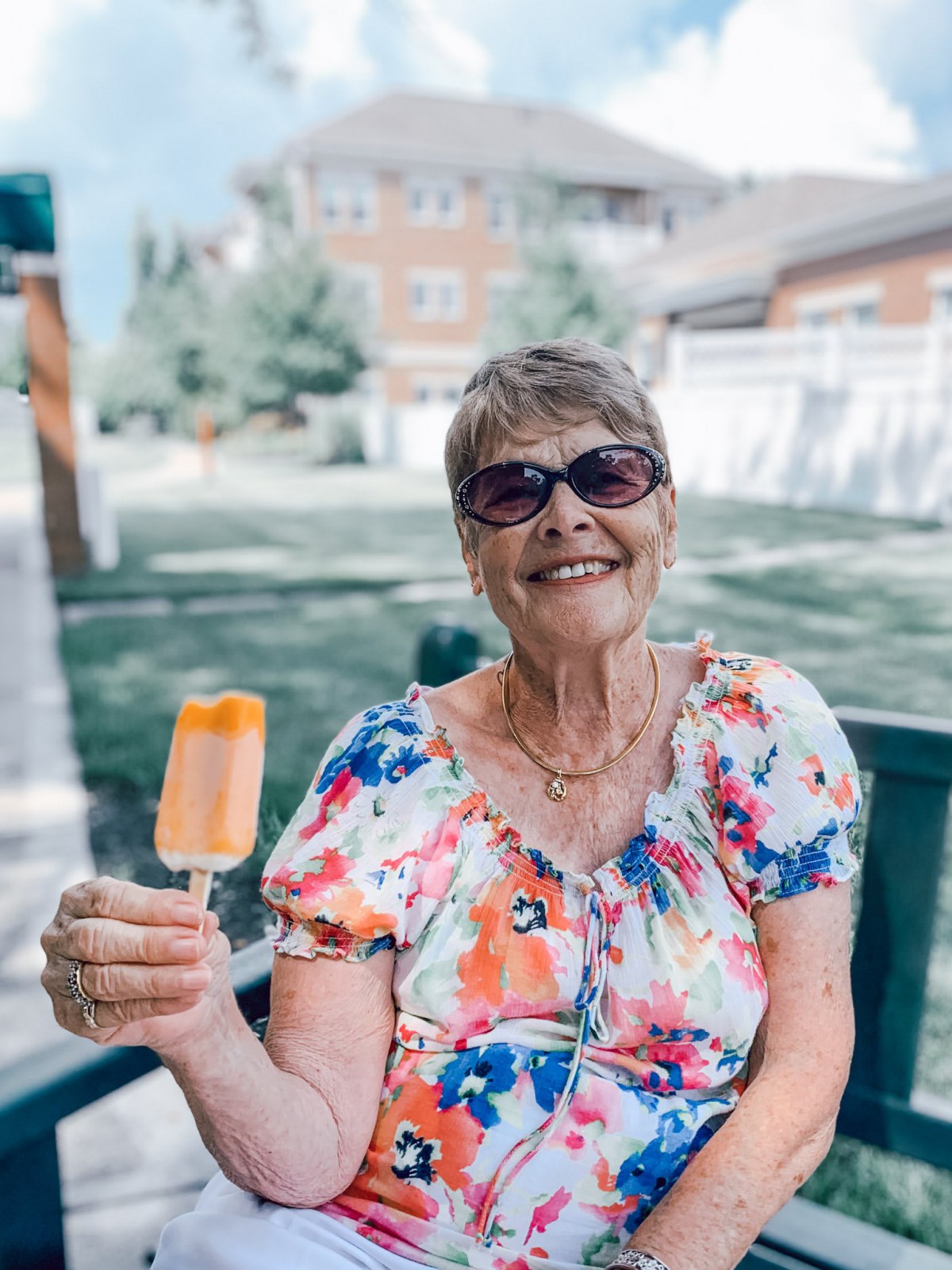 A cheerful elderly woman enjoys an ice pop outside on a sunny day.