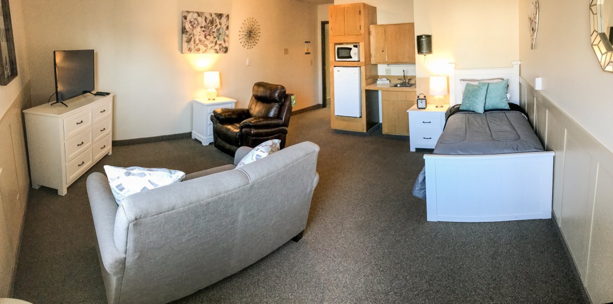 A cozy living room with comfortable seating and a small kitchenette in the background.