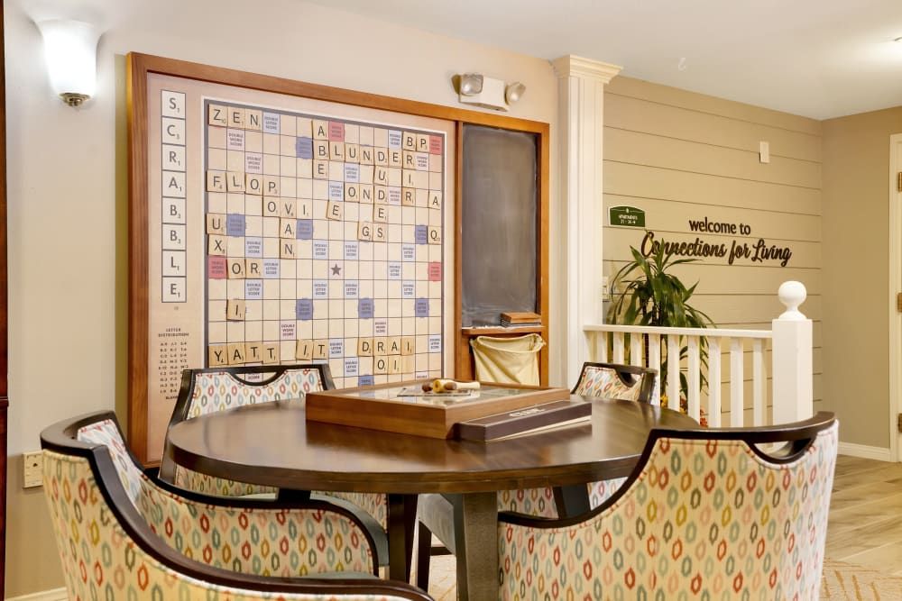 A cozy game room featuring a large Scrabble board on the wall, surrounded by a table and chairs for playing board games.