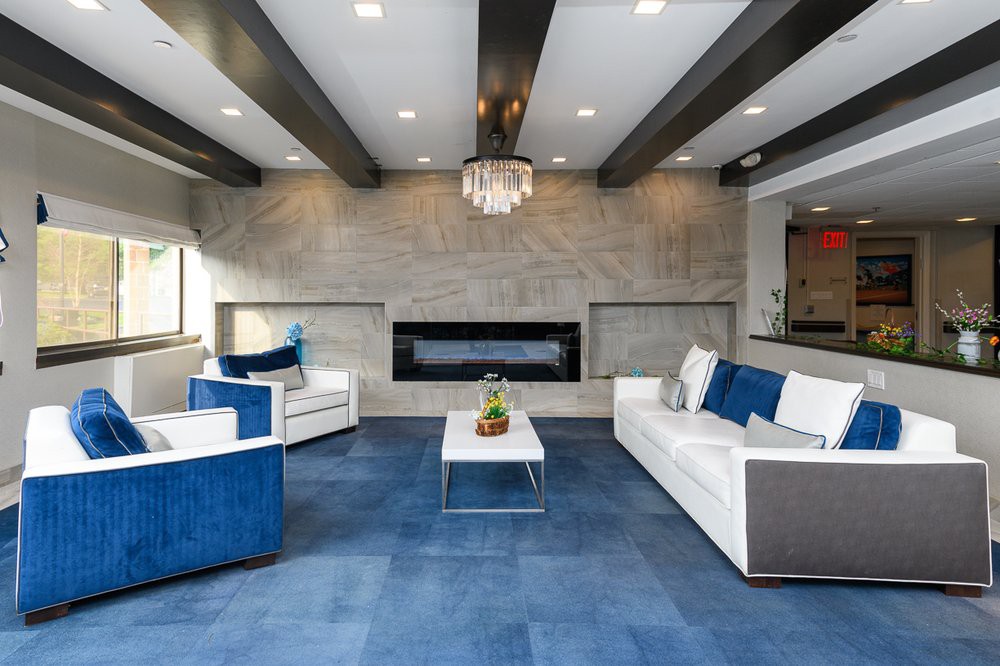 A modern living room with blue carpeting, white furniture, and a sleek fireplace.