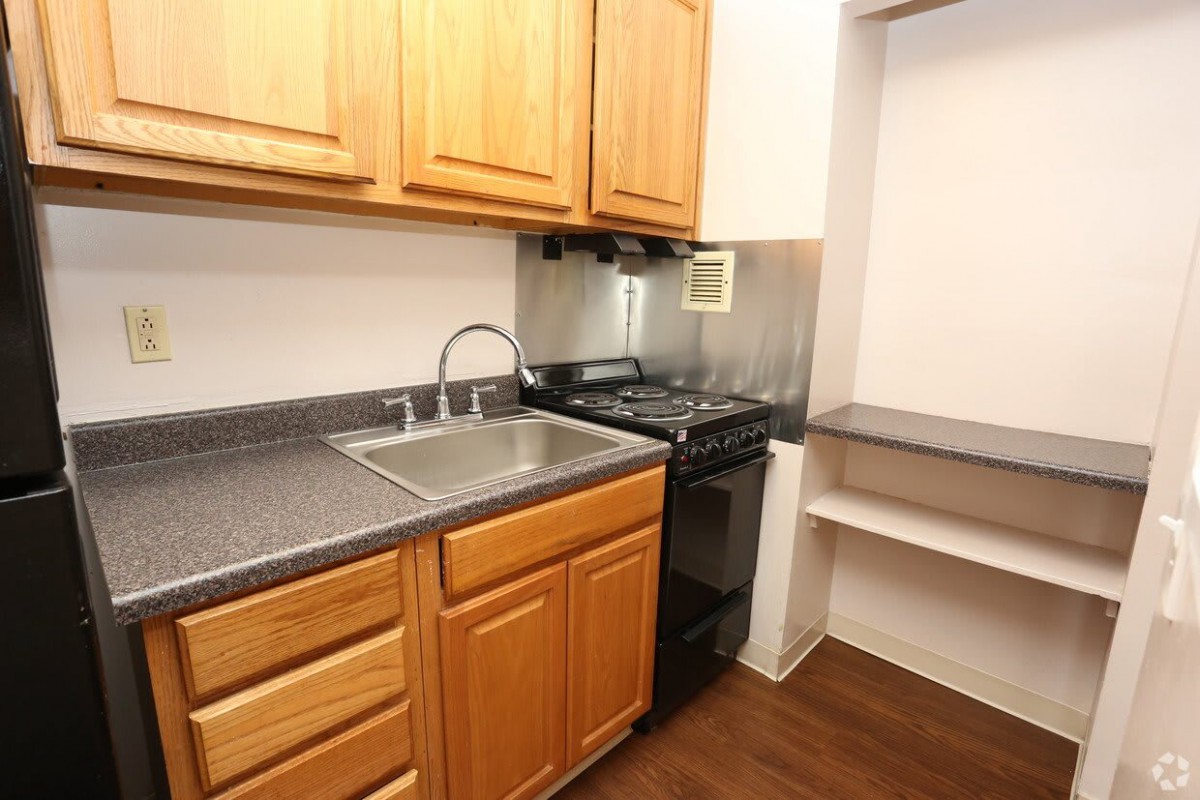 A compact kitchen with wood cabinets, a stainless steel sink, and a stove.