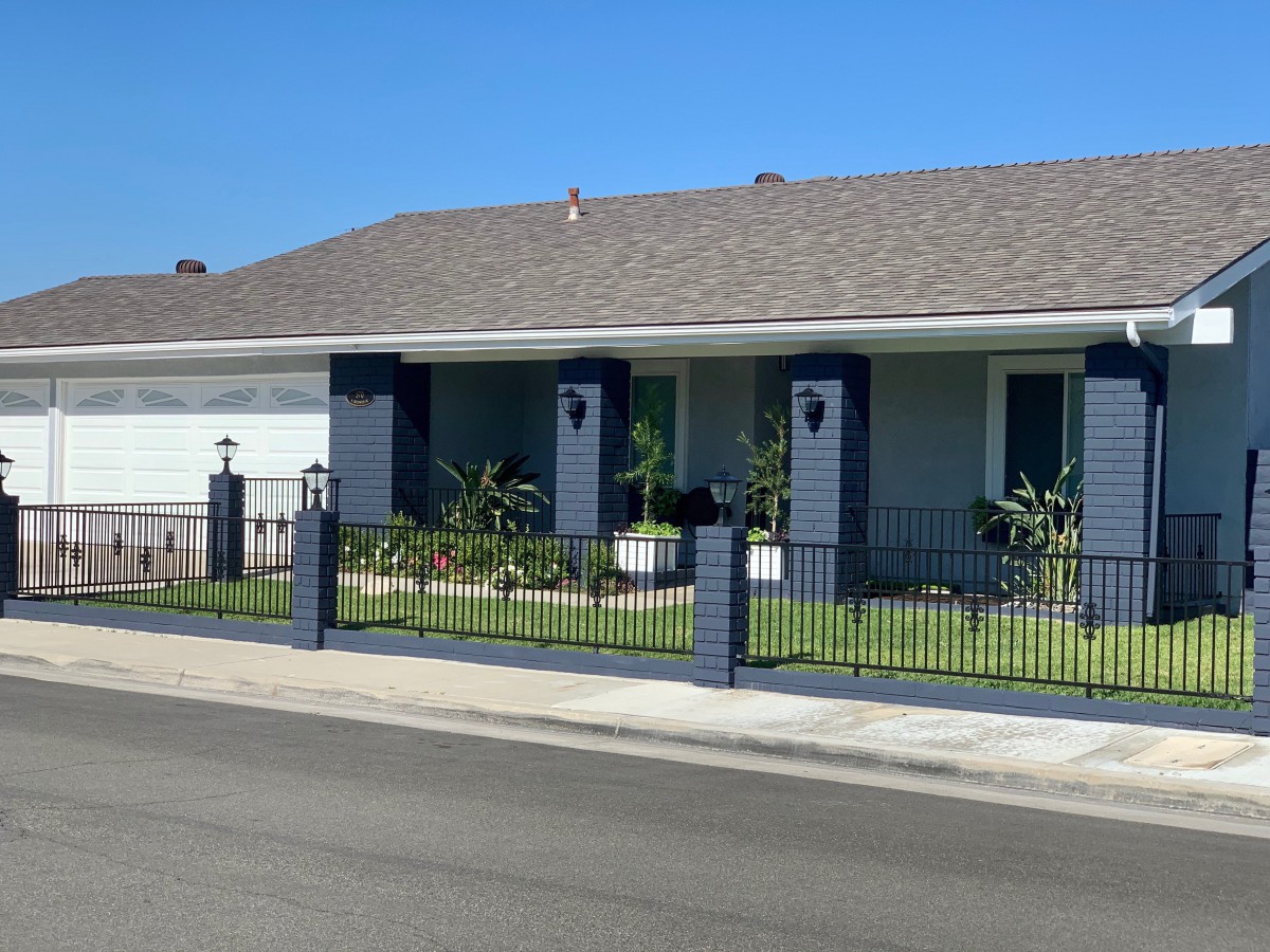 A single-story house with a fenced front yard under a clear blue sky.
