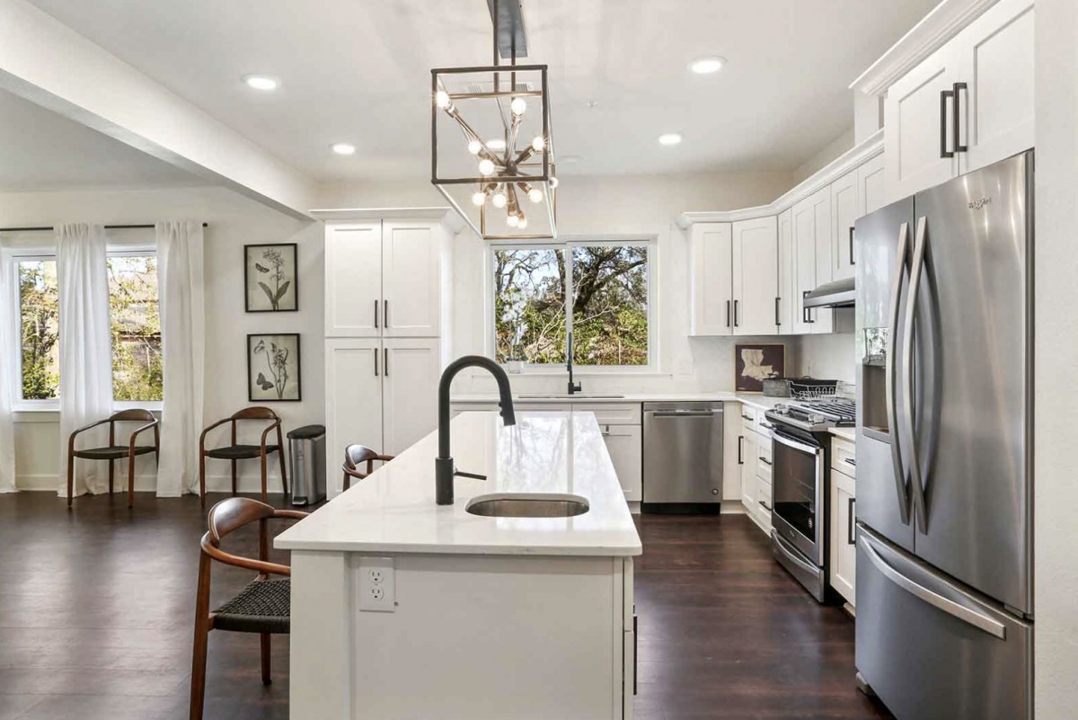 A modern kitchen featuring white cabinets, an island, stainless steel appliances, and pendant lighting over a hardwood floor.
