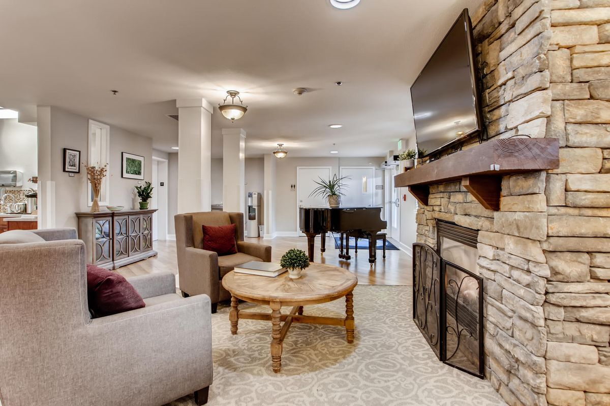 A cozy living room with a fireplace, TV, and piano, featuring modern decor and comfortable seating.