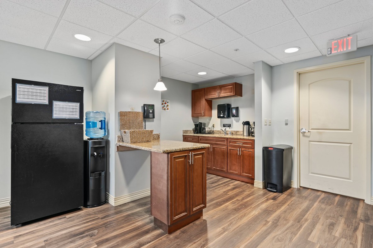 A modern office kitchen featuring a refrigerator, water cooler, and wooden cabinetry.