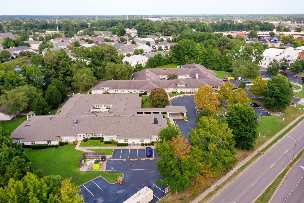 Aerial view of a suburban area with buildings, a parking lot, and lush green trees.