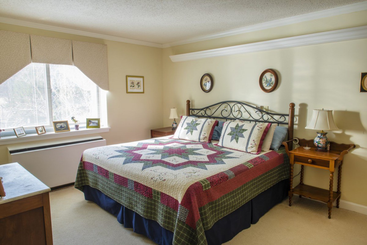 A cozy bedroom with a large bed covered in a patchwork quilt, featuring traditional decor and soft lighting.