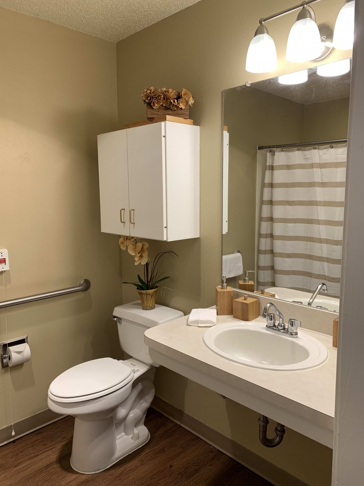 A tidy bathroom with beige walls, featuring a sink, mirror, toilet, and shower area.