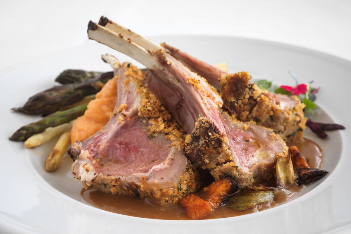Herb-crusted rack of lamb served with assorted vegetables.