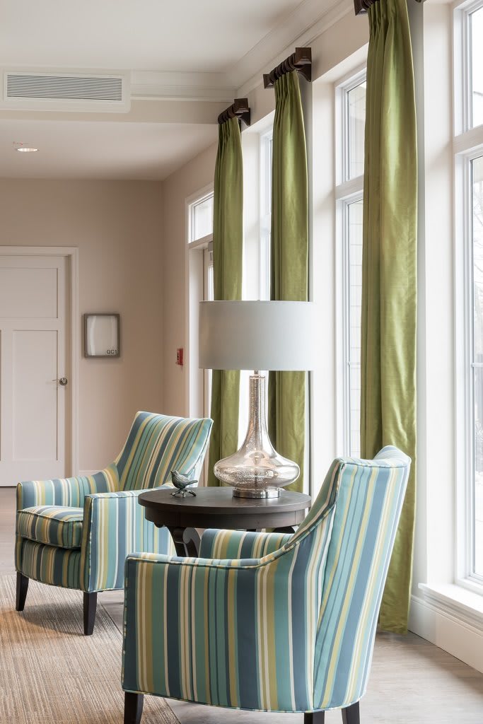 A cozy living room corner with striped chairs, a lamp, and green curtains.