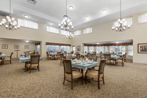 A spacious and elegantly decorated dining room with multiple tables and chandeliers.