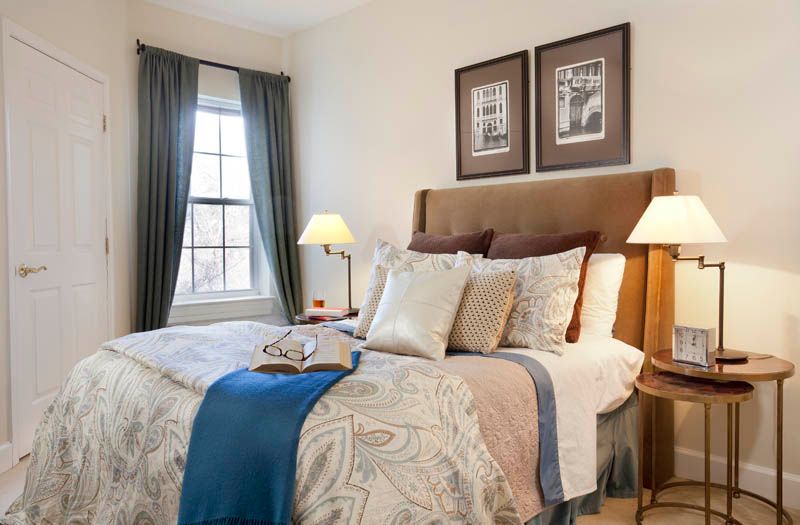 A cozy and well-decorated bedroom featuring a neatly made bed with patterned bedding, flanked by lamps on wooden nightstands and adorned with framed artwork on the wall.