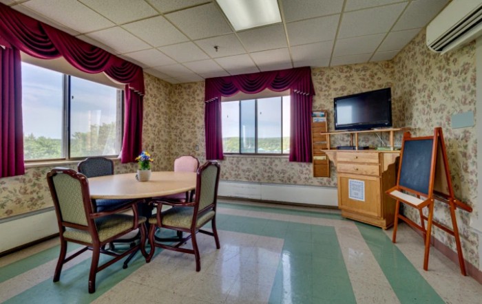 A small conference room with a round table, chairs, television, and large windows that provide ample natural light.