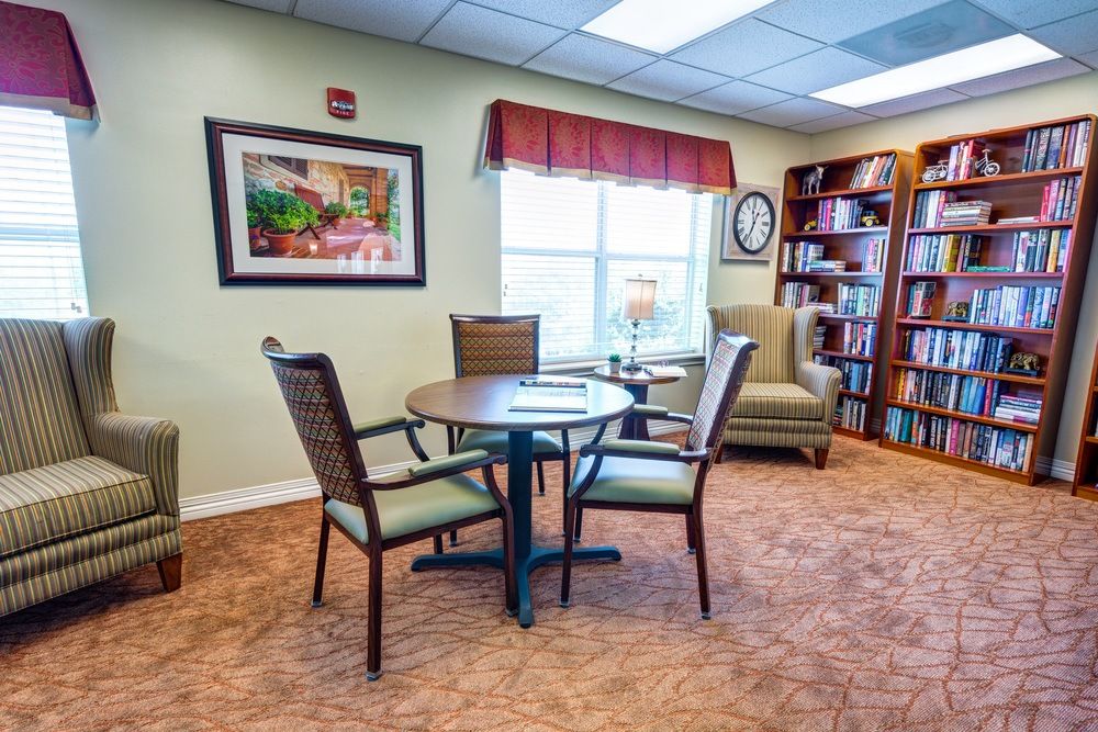 A cozy reading room with a table, chairs, and a bookshelf by the window.