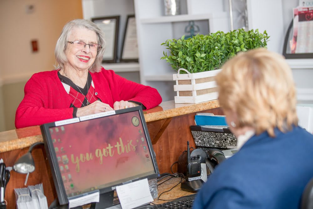 A woman at a reception desk engaging with a visitor in an office environment.