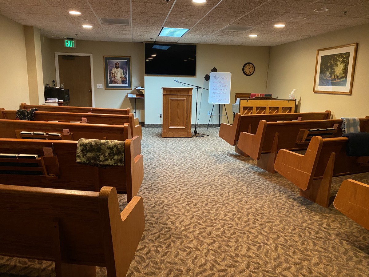 An interior view of a small room with wooden pews and a podium at the front, resembling a chapel or worship space.