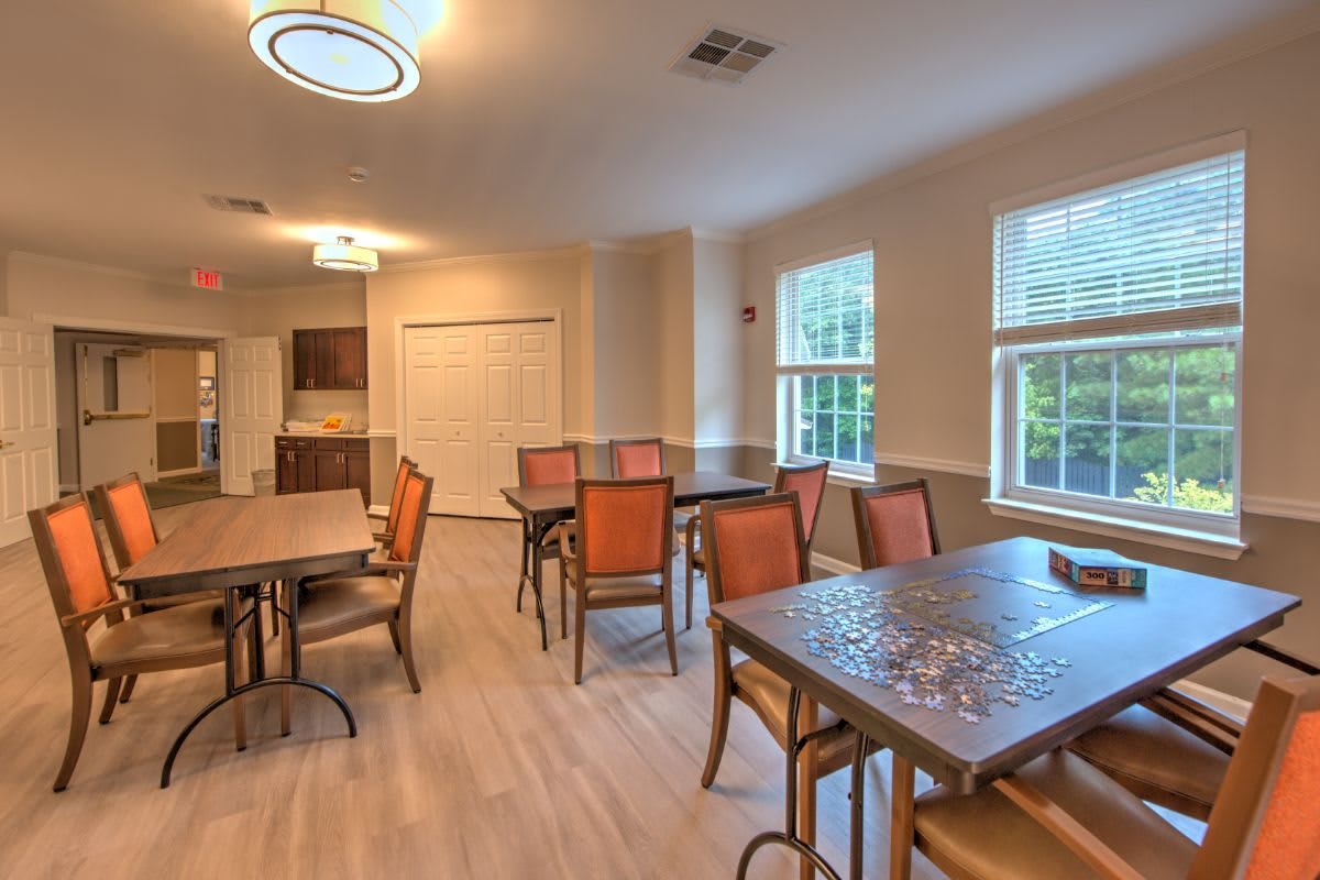 A well-lit dining area with multiple tables and chairs, adjacent to a kitchen space.