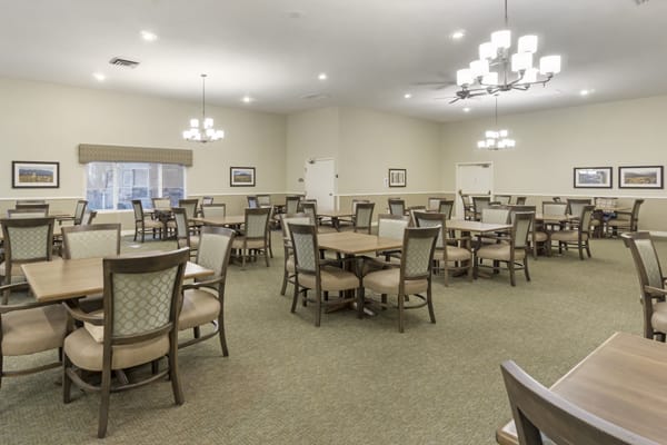 An empty dining room with multiple tables and chairs, well-lit with overhead lights.