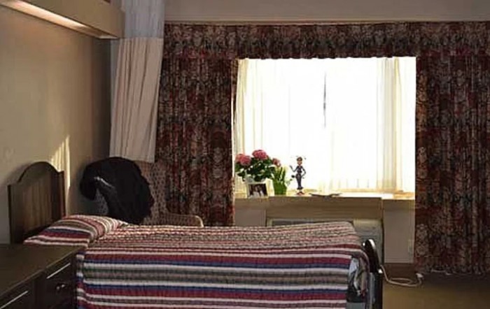 A cozy bedroom featuring a neatly made bed and a window with floral curtains, allowing natural light to brighten the room.