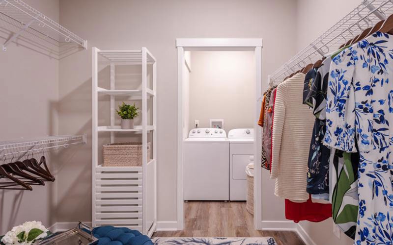 A laundry area with a washer and dryer, adjacent to a closet with hanging clothes.