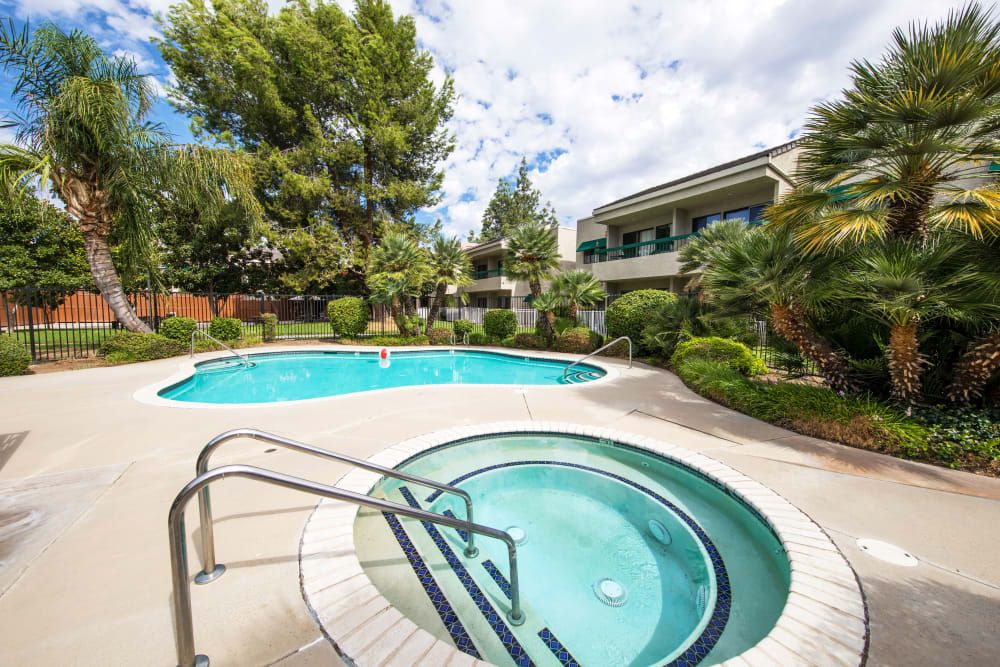 A scenic view of a residential outdoor area with a swimming pool and hot tub surrounded by lush greenery.