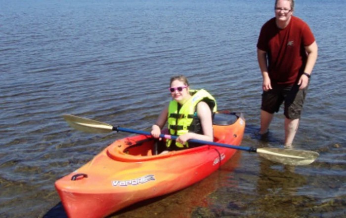 A person in a kayak wearing a life jacket with a paddle on a lake.