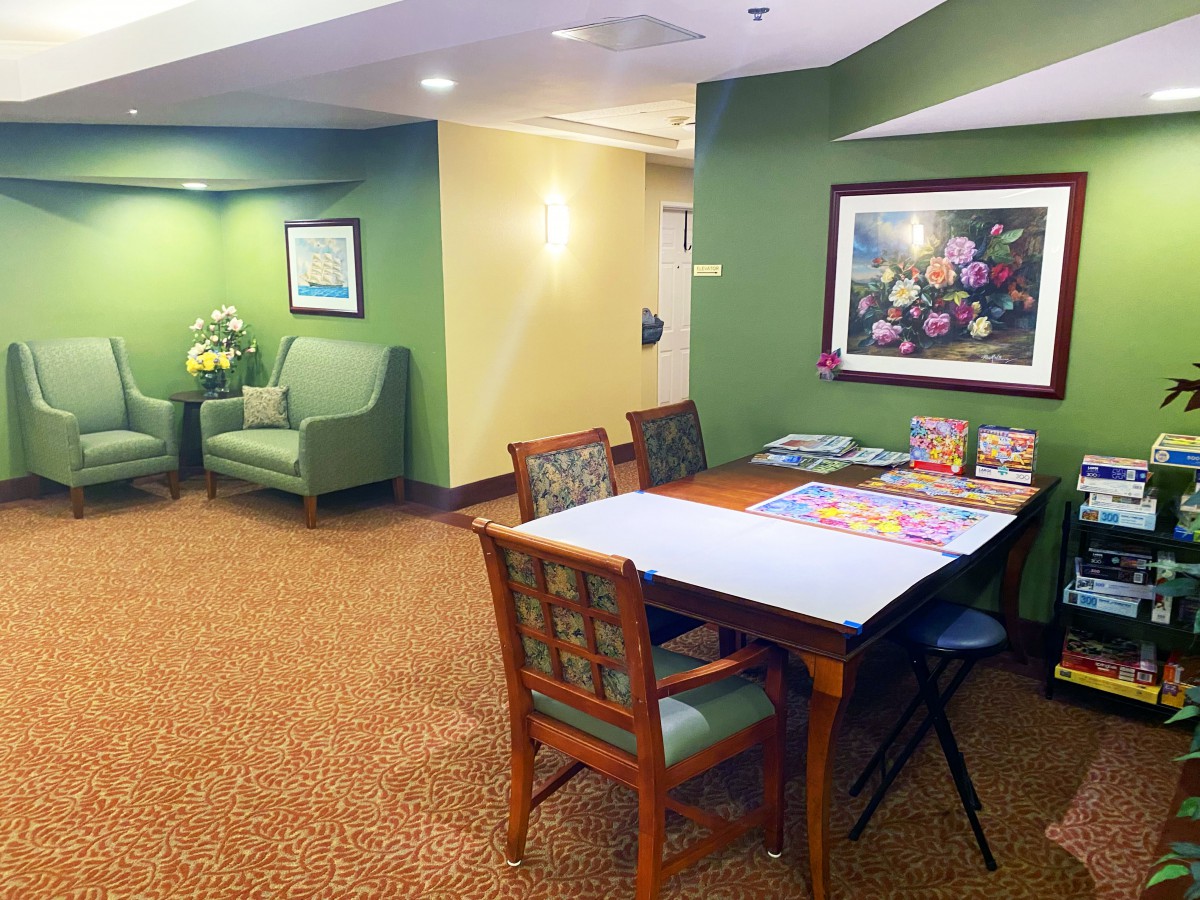 A cozy waiting room with green walls, comfortable seating, and a table with chairs, adorned with artwork and magazines.