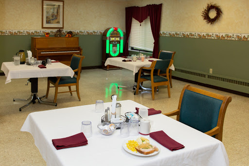 A cozy dining area set for a meal, featuring tables with white tablecloths and food items, alongside a piano in the background.