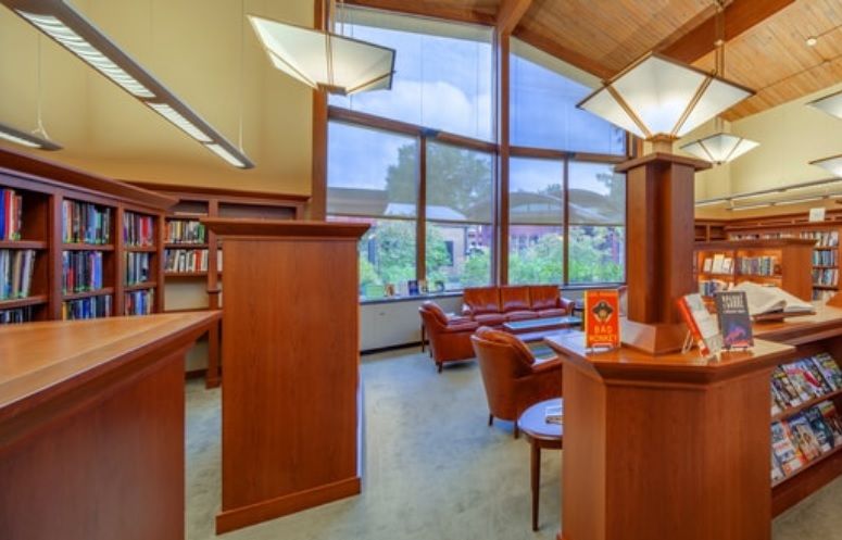 A cozy library with wooden furniture and large windows letting in natural light.