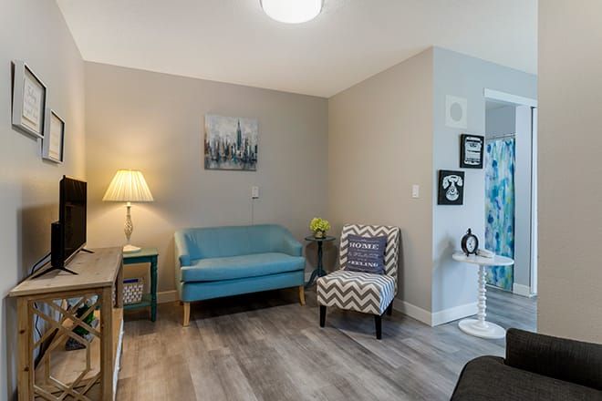 A cozy living room with modern decor, featuring a blue sofa, patterned armchair, and ambient lighting.