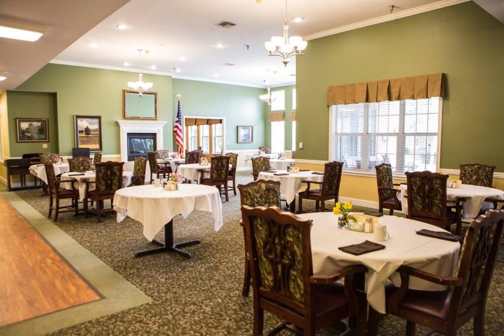 An elegant dining room with neatly arranged tables and chairs, featuring chandeliers and tasteful decor.