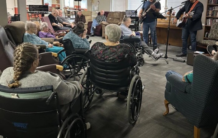 Elderly residents in wheelchairs enjoy a live music performance at a nursing home.