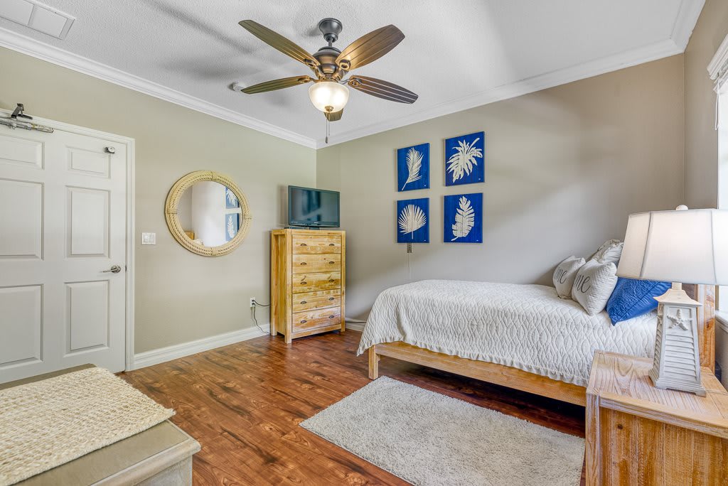 A modern bedroom with wood flooring, neutral colors, and a ceiling fan features decorative artwork and simple furnishings.
