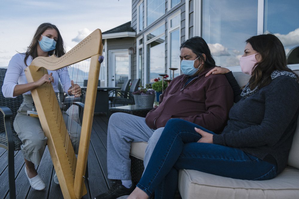 A group of people wearing masks sit outside while one person plays a harp.