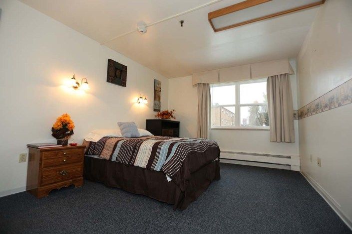 A cozy bedroom featuring a neatly made bed, nightstand with a lamp, and a large window with curtains.