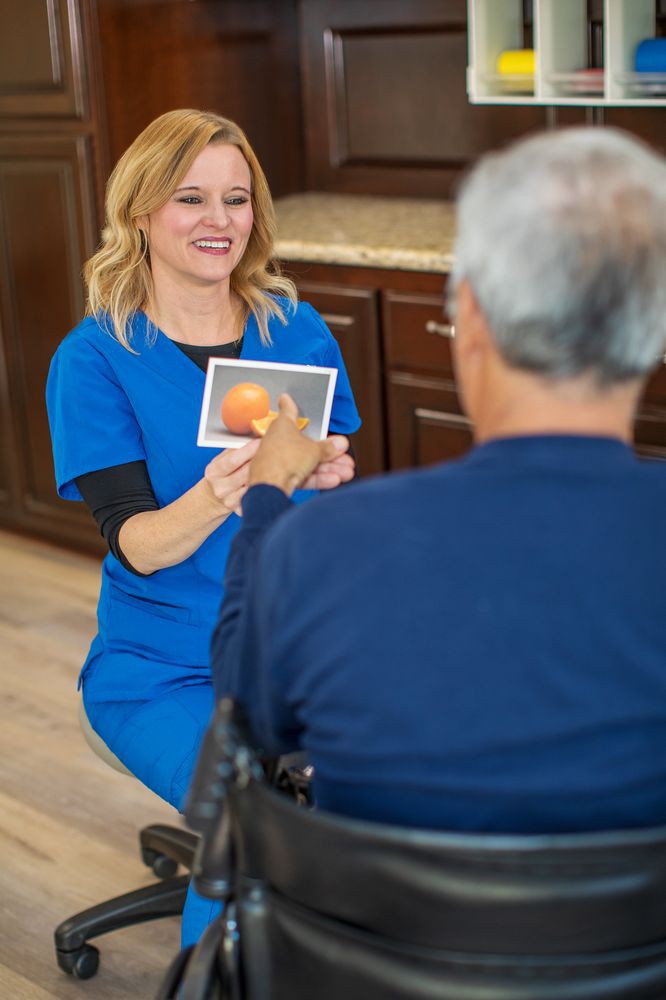 A healthcare professional interacts with an elderly person, holding up a card for communication.