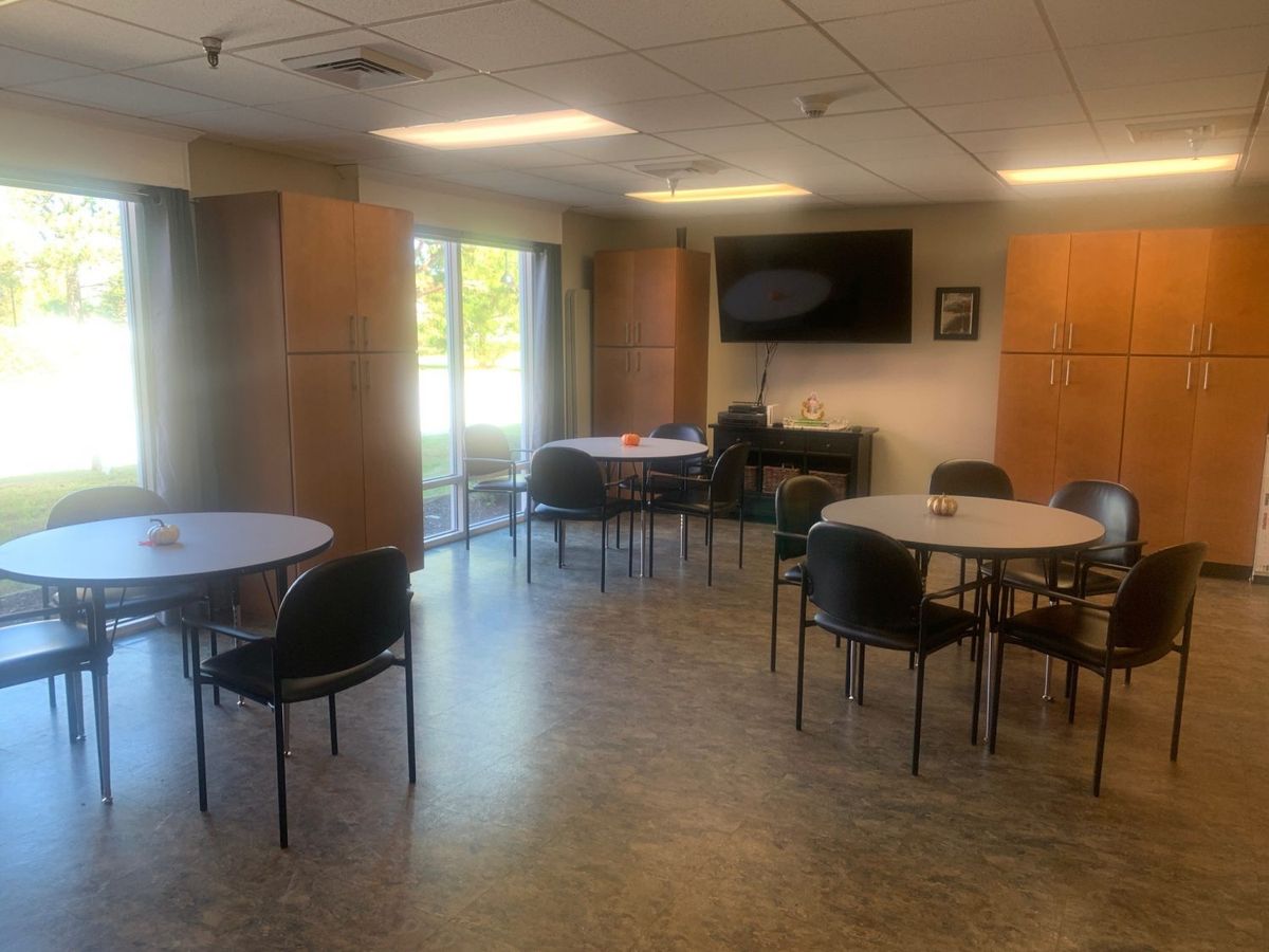 A spacious break room with round tables, chairs, and a wall-mounted television.
