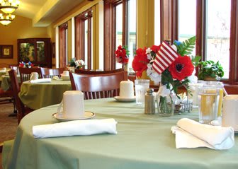 A restaurant dining area with tables set for guests, featuring floral arrangements and a small American flag.