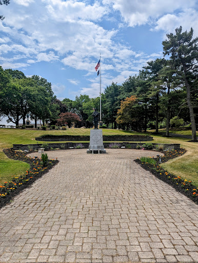 A serene park setting featuring a memorial monument surrounded by neatly arranged flower beds and a flagpole.