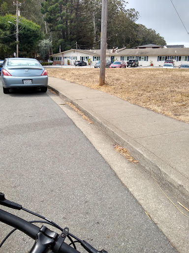 A view of a street with parked cars and a residential area in the background.