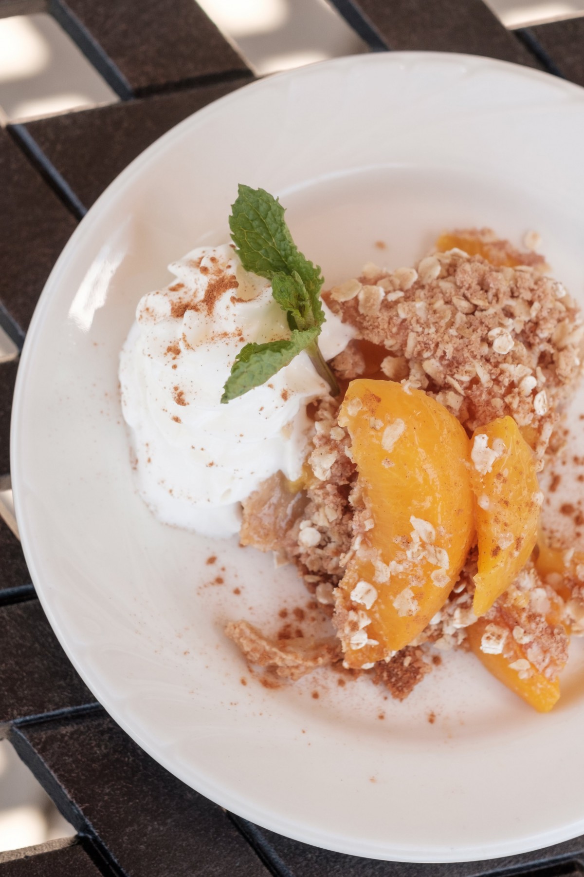 A delectable serving of peach crumble with whipped cream and a mint garnish.