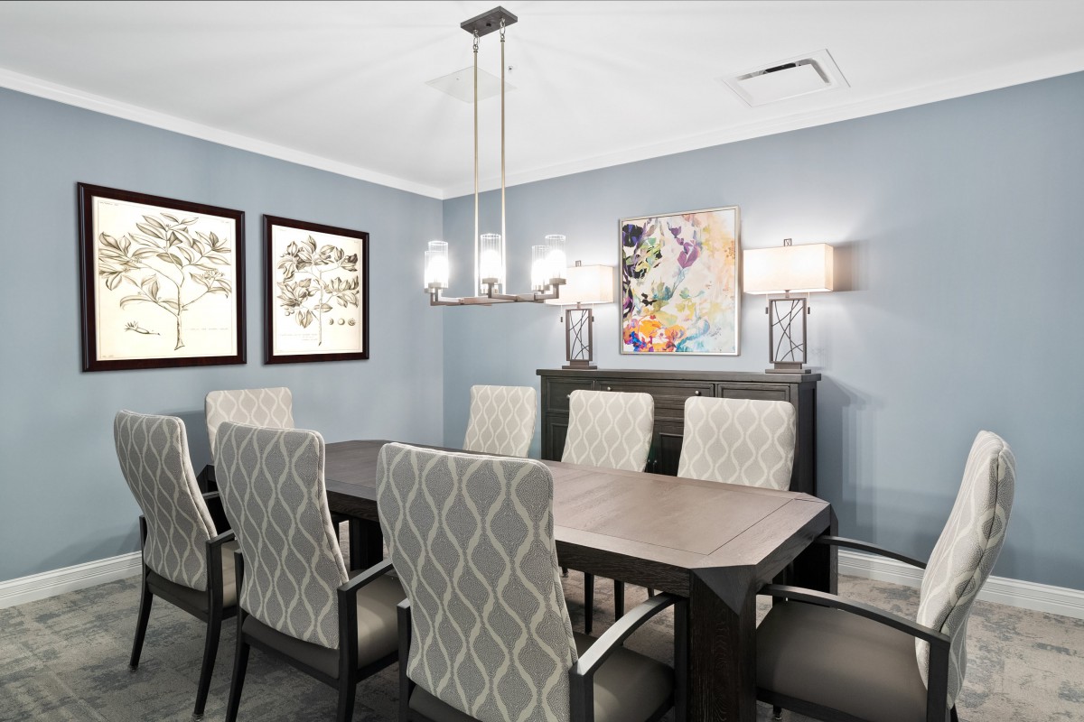 A modern dining room with a large table, patterned chairs, artwork on the walls, and a stylish chandelier.