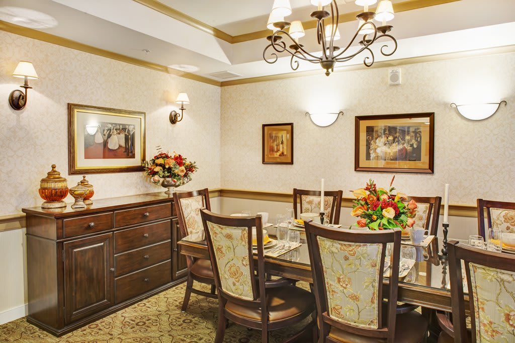 A warmly decorated dining room with a wooden table and chairs, adorned with floral arrangements and artwork on the walls.