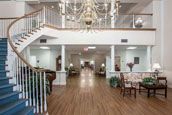 A spacious interior with a central chandelier, staircase, and hallway leading to various rooms.