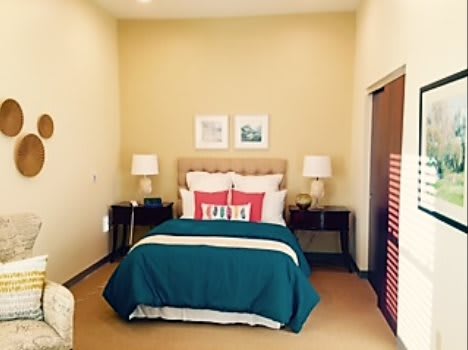 A neatly arranged bedroom featuring a double bed with teal bedding, flanked by matching nightstands and lamps.