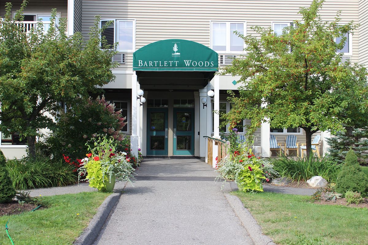 The entrance of a building with a green awning labeled 'Bartlett Woods', surrounded by plants and trees.